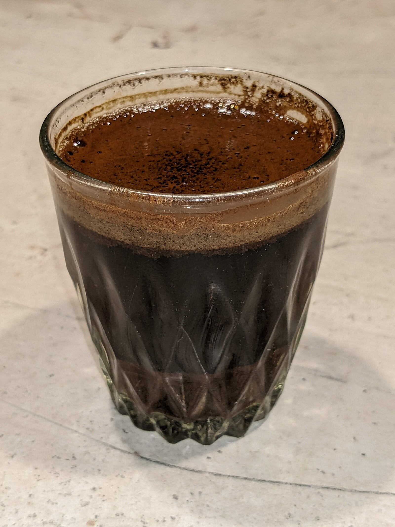 A clear glass of dark Czech-style “turek” coffee with grounds/sediment visible.