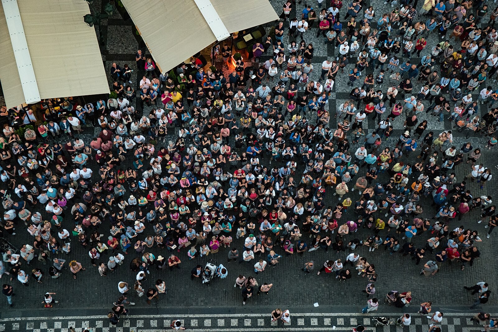 Overhead view of a dense tourist crowd and café/restaurant frontage on Old Town Square.