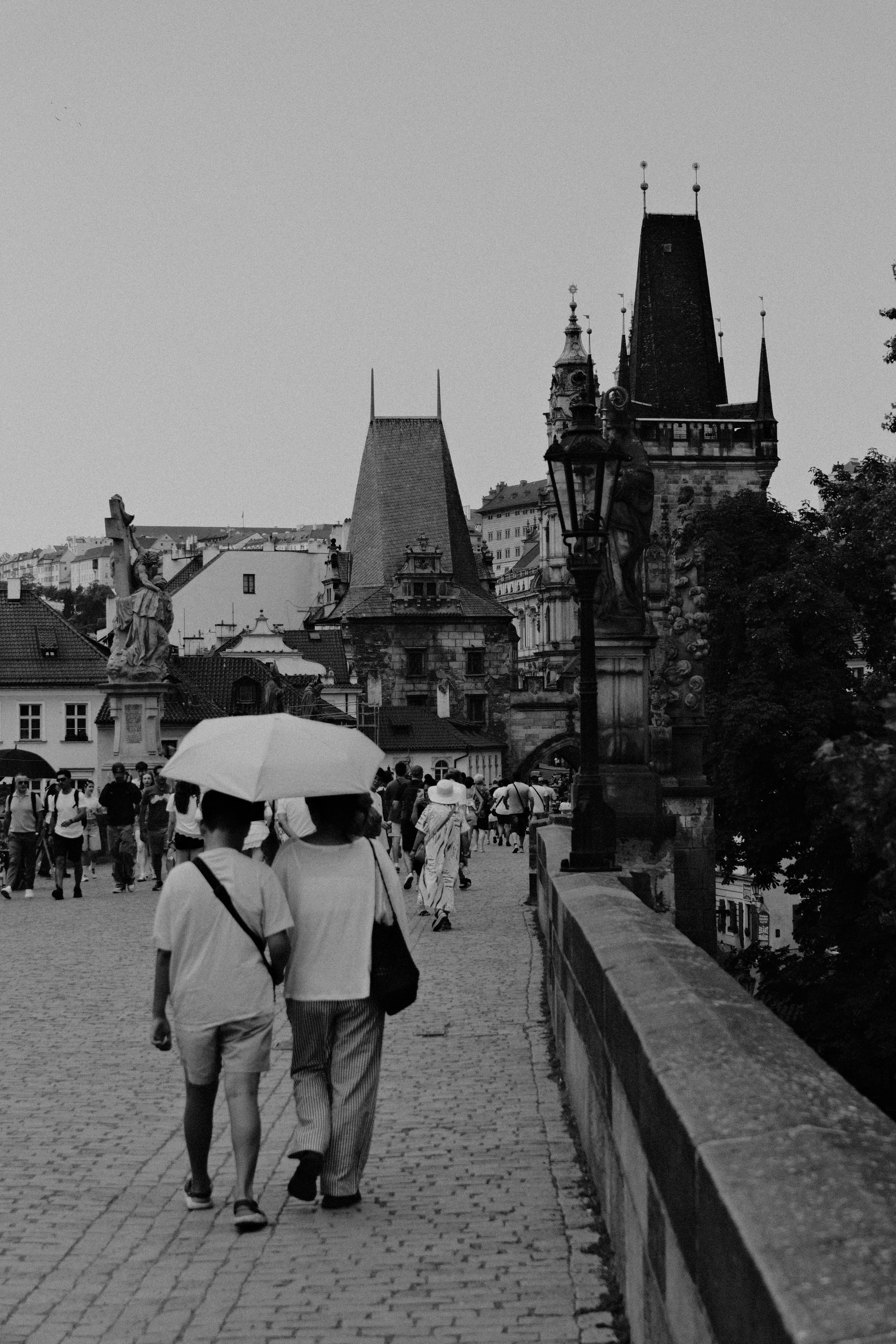People with umbrellas walking on Charles Bridge in visibly rainy/wet conditions.
