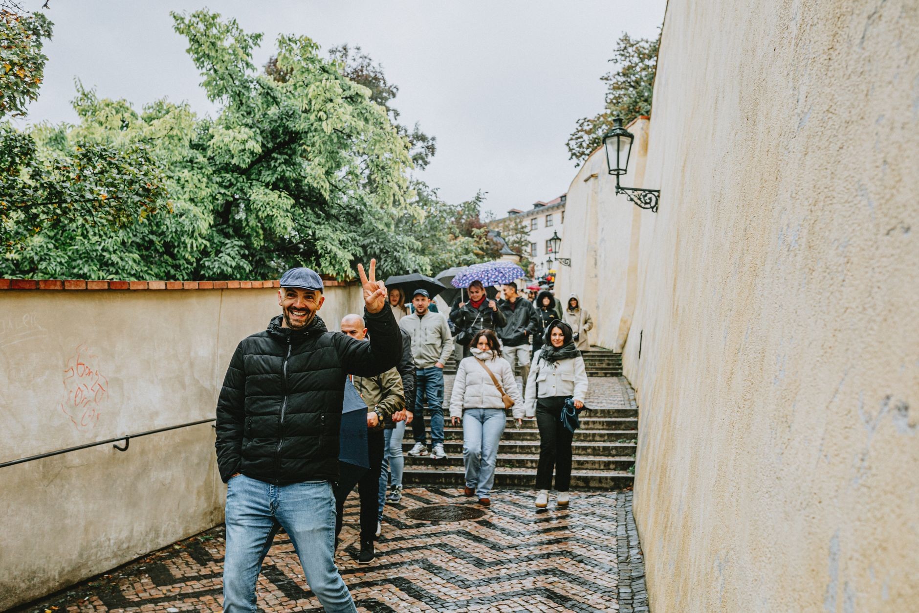 Visitors walking Prague steps in wet weather, with umbrellas/rain context.