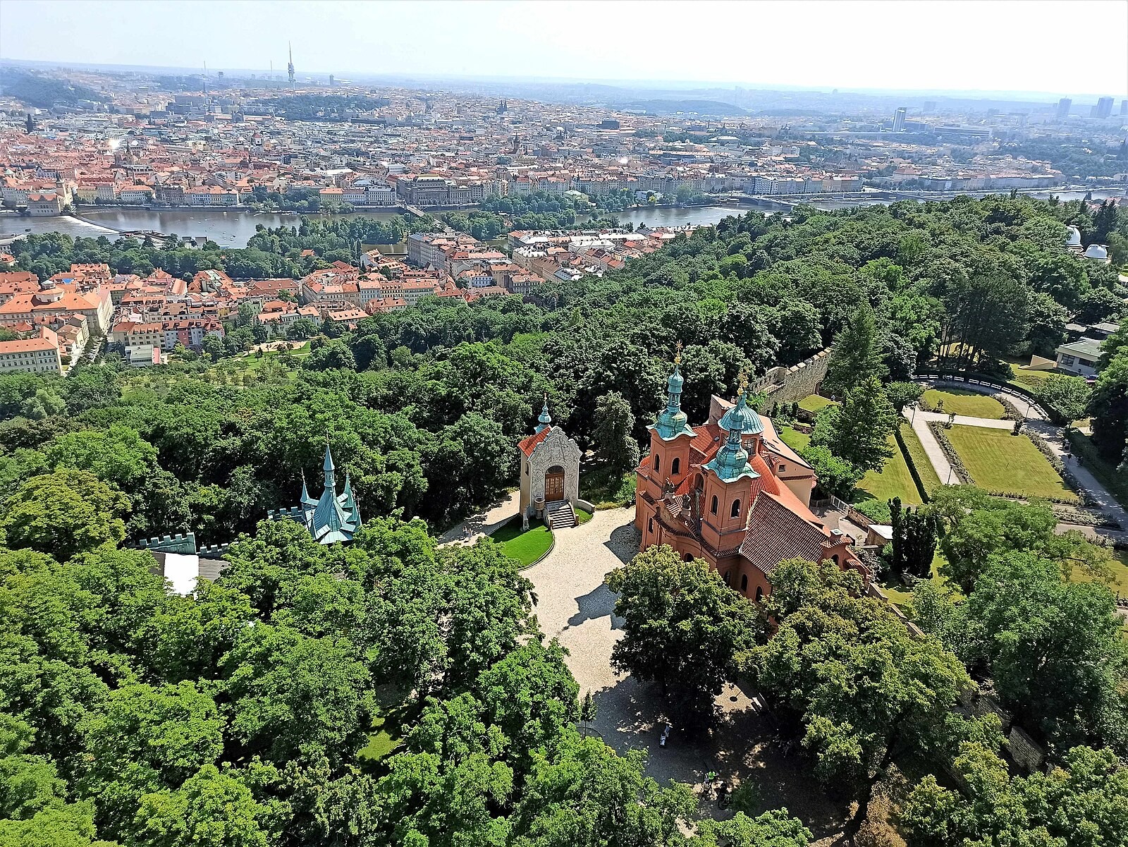 Wide Prague cityscape seen from the Petřín area, including greenery and central landmarks.