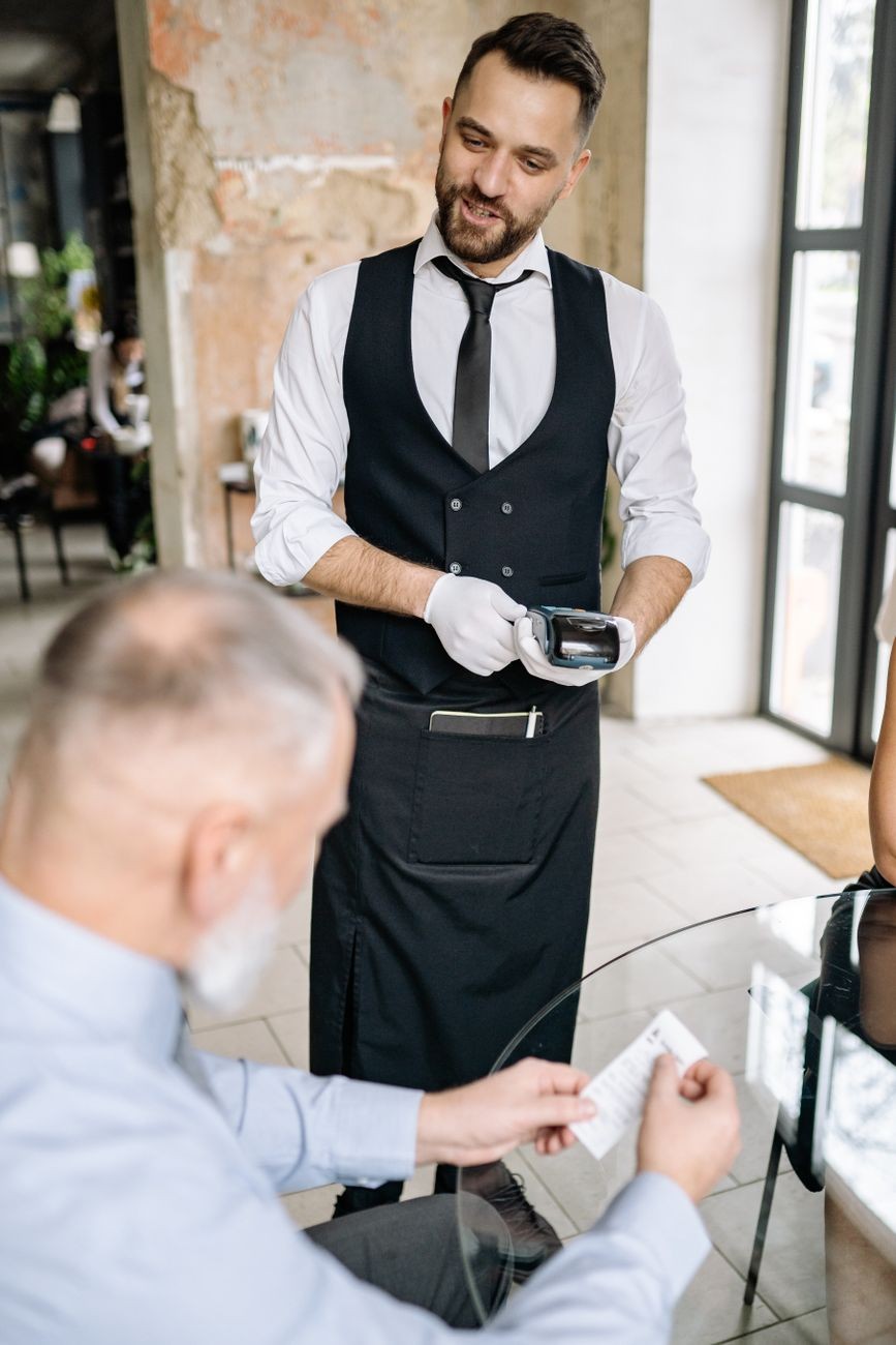 Waiter processes card payment while a customer reviews the bill.