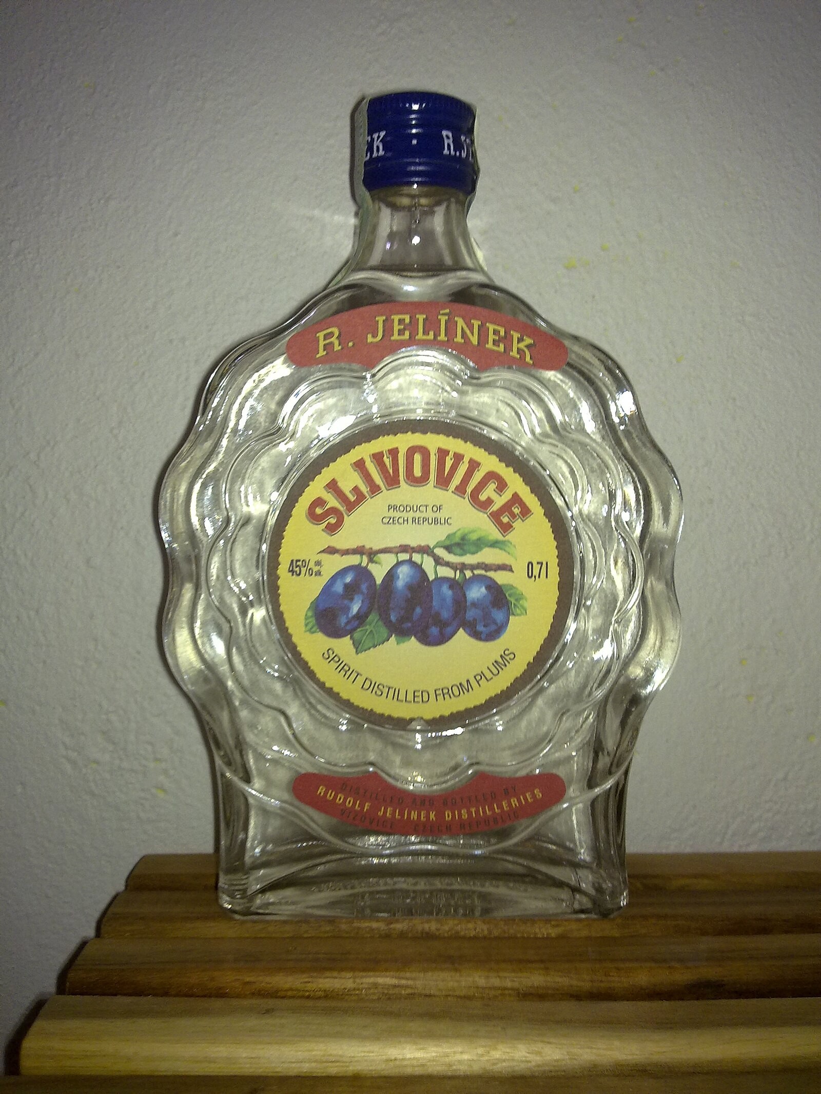 Bottle of Rudolf Jelínek slivovice with plum imagery and product label clearly visible.