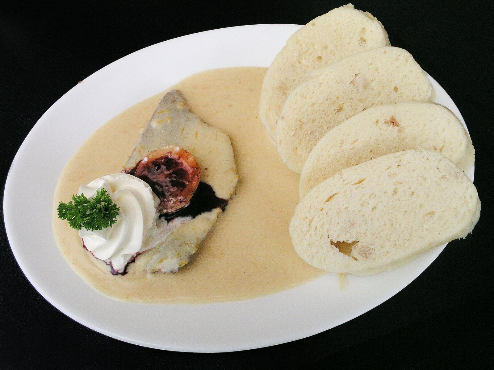Svíčková with cream sauce, bread dumplings, lemon and cranberries all visibly present.