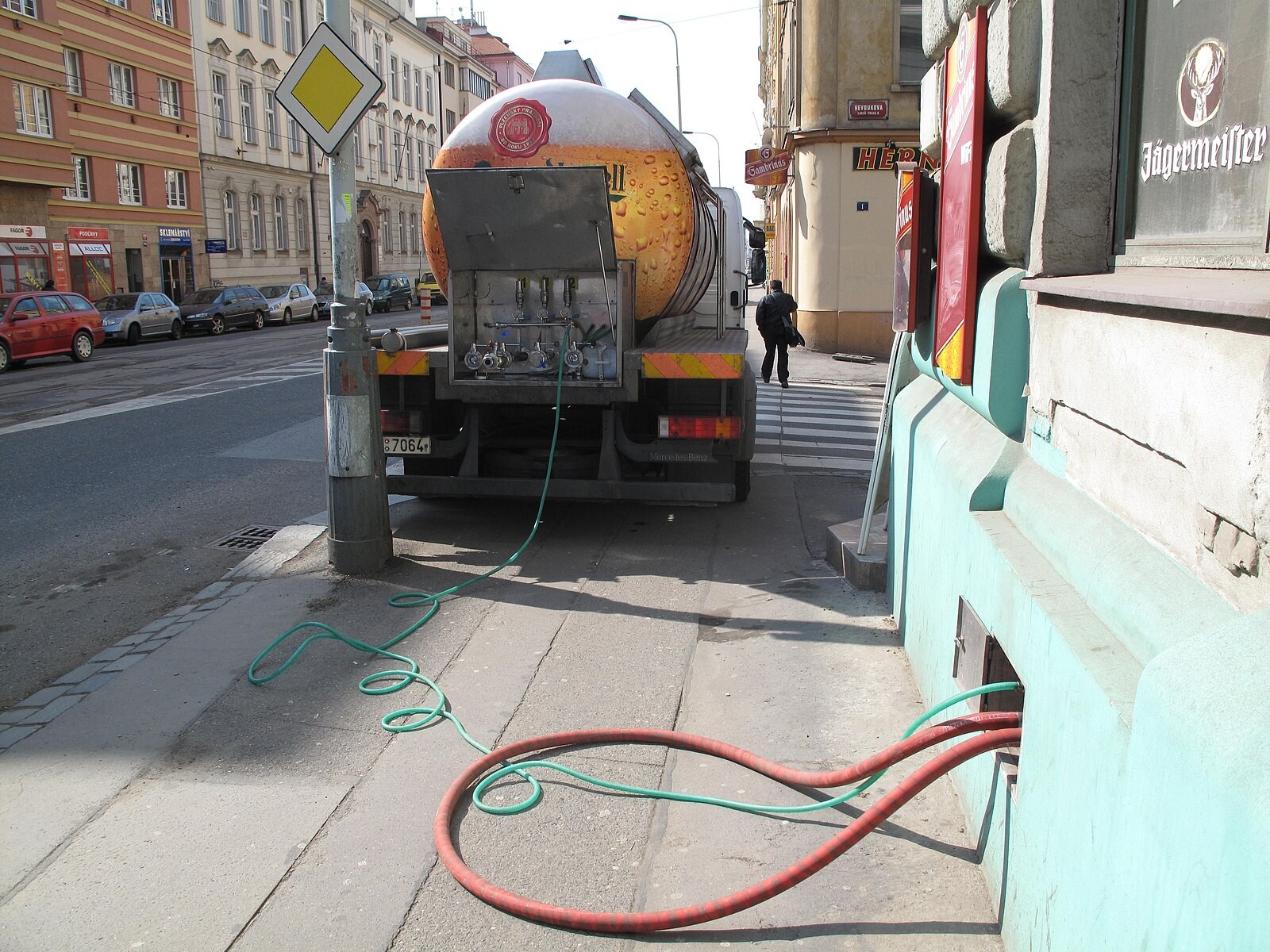 Pilsner beer tanker truck on a Prague street with delivery hoses running into a building/pub cellar.