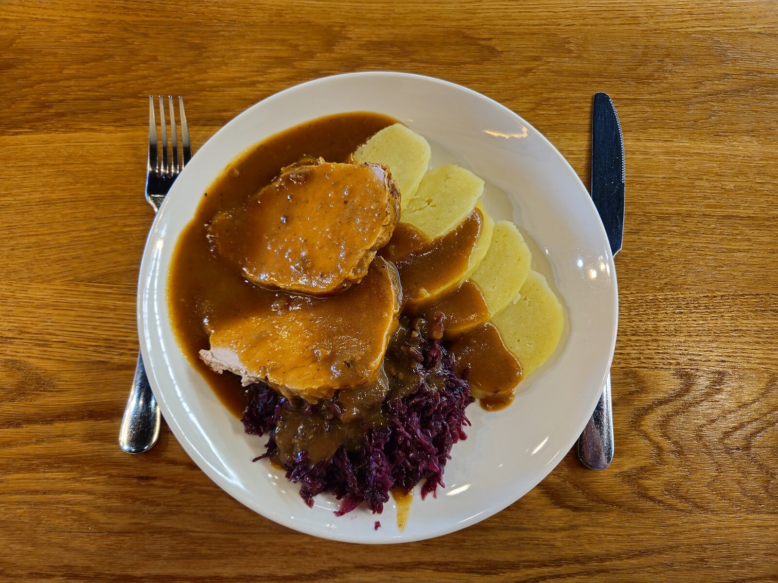 Plate showing roast pork, bread dumplings, cabbage and gravy together.