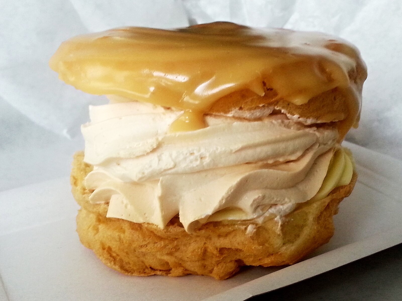Close-up of a větrník showing choux pastry, caramel glaze and two visibly distinct cream layers.