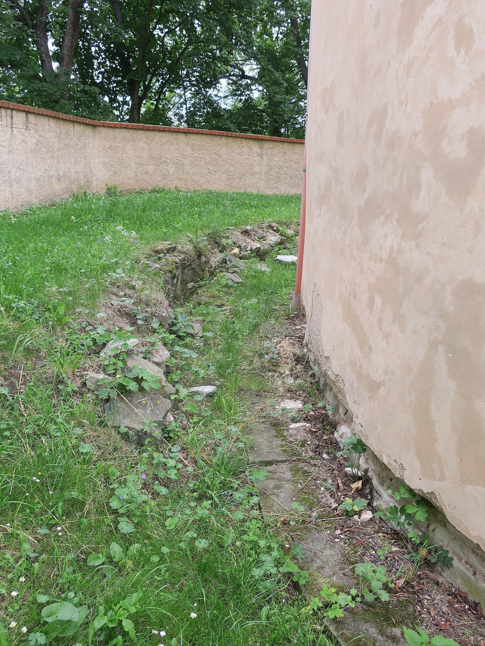 Low stone foundations/remains of an apse at the archaeological site, showing Budeč beyond the standing rotunda.