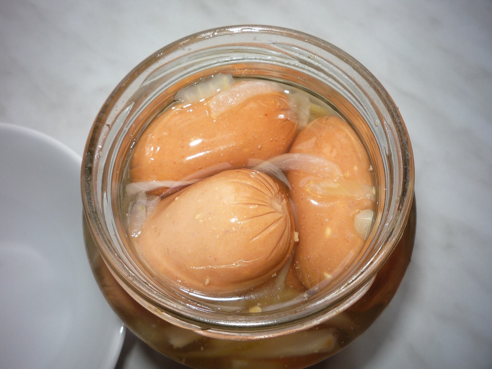 Close-up of small utopenci in a glass jar with pickling ingredients.
