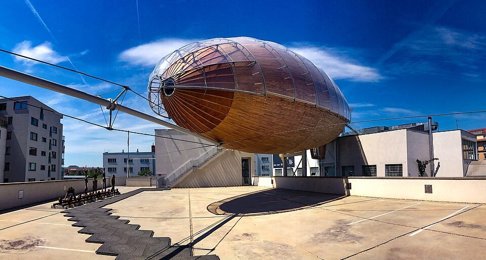 Full external side/bow view of the rooftop airship against blue sky.