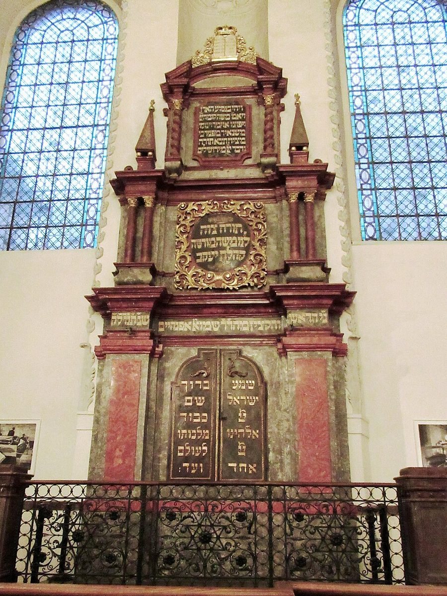 Frontal portrait of a richly decorated Torah ark between tall windows.