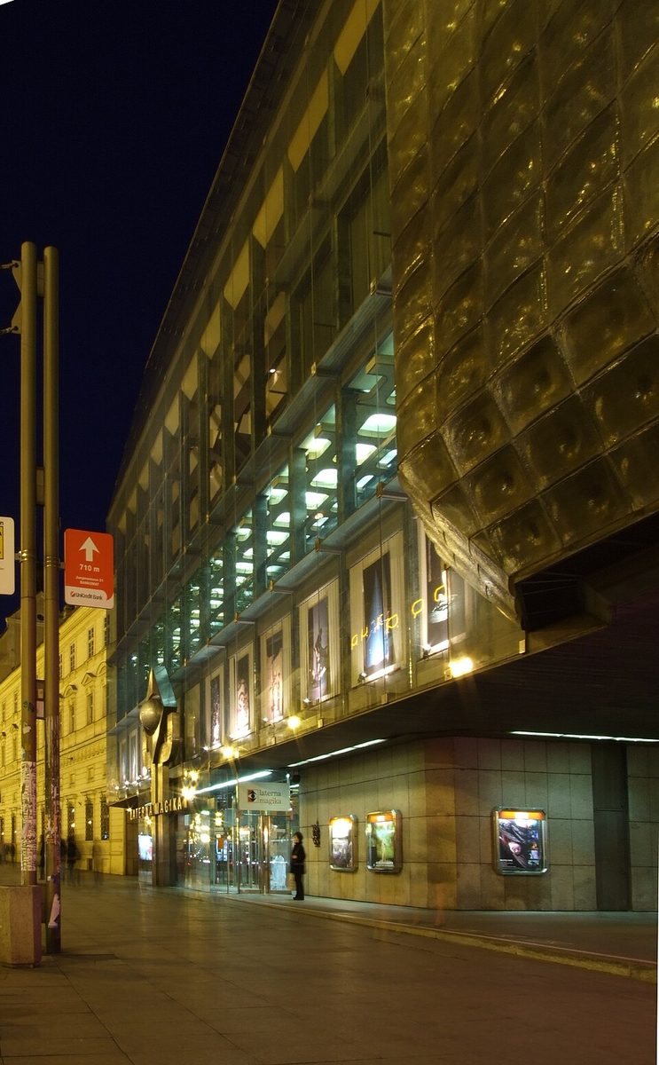 Tall nighttime street view of the glass-and-metal Laterna Magika/New Stage façade.