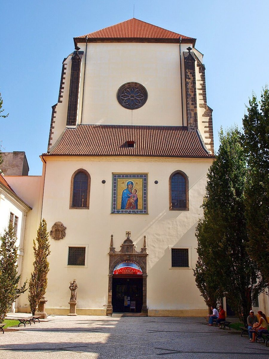 Centered daylight façade with round window, icon above entrance and red roof.