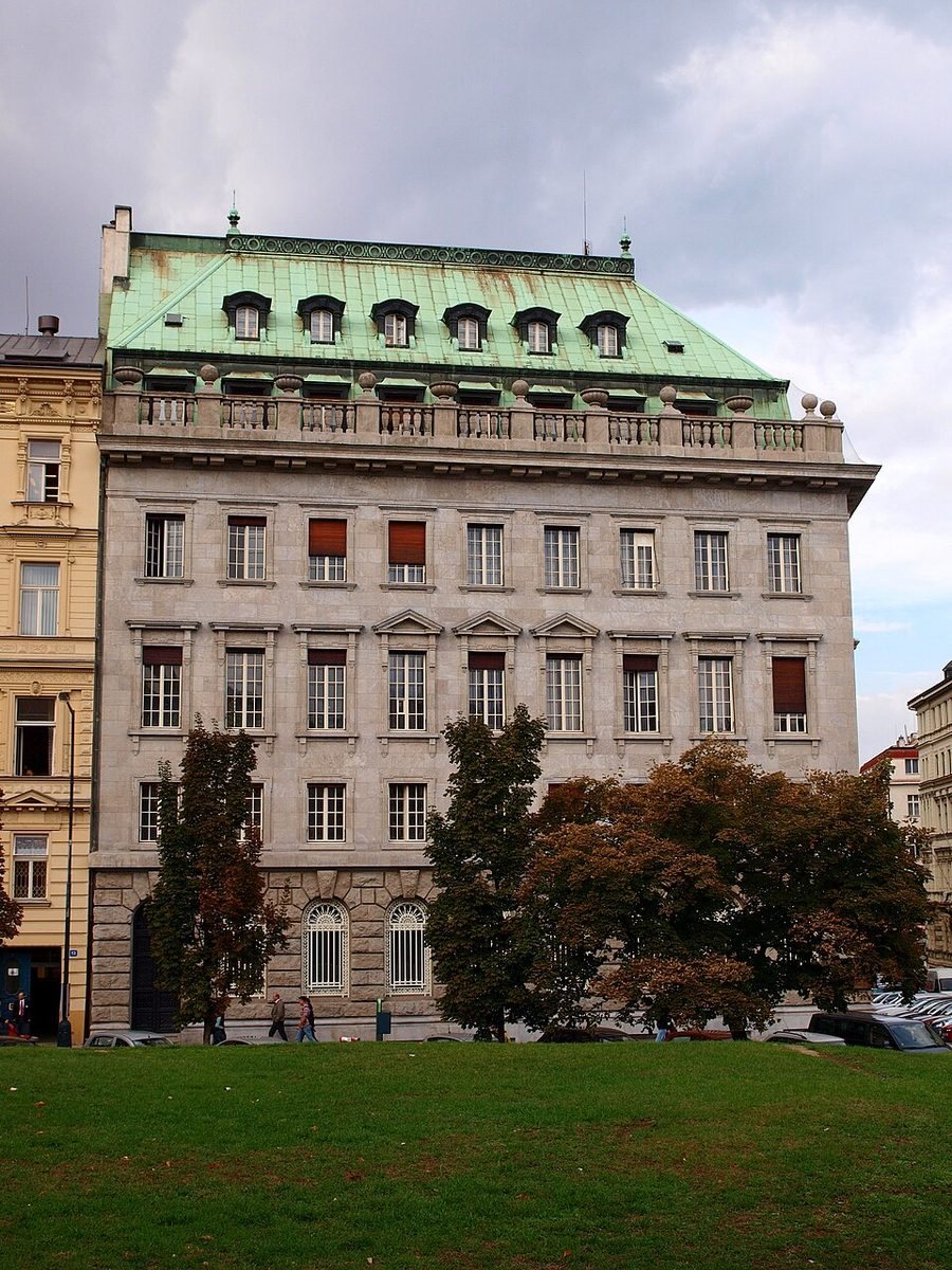 Clear portrait exterior of the large pale stone Petschek Palace with green roof.