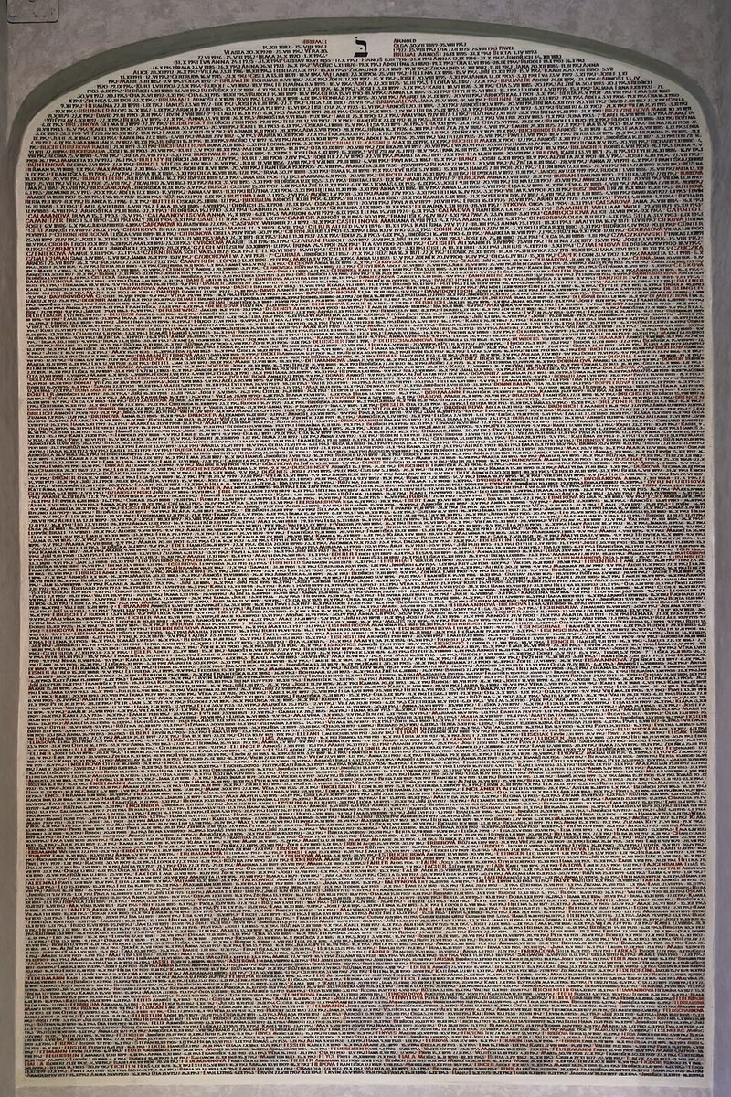 Large arched wall panel densely filled with victims’ names, framed cleanly and frontally.