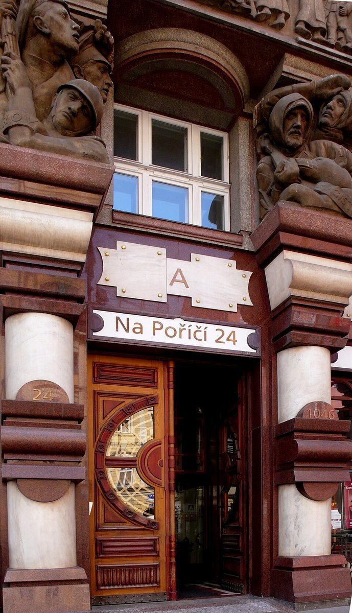 Tight portrait of the entrance showing cylindrical columns, carved figures and the address plaque.