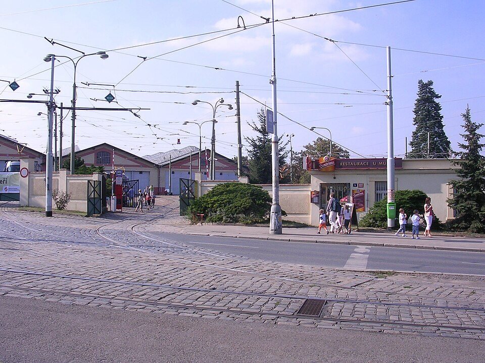 Wide exterior of the depot entrance, tracks, overhead wires and visitors.