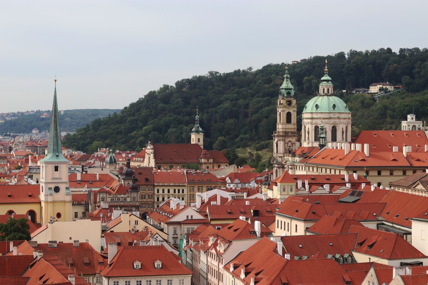 Elevated roofscape visibly shows the St Nicholas dome and adjacent tower rising separately above Lesser Town roofs.