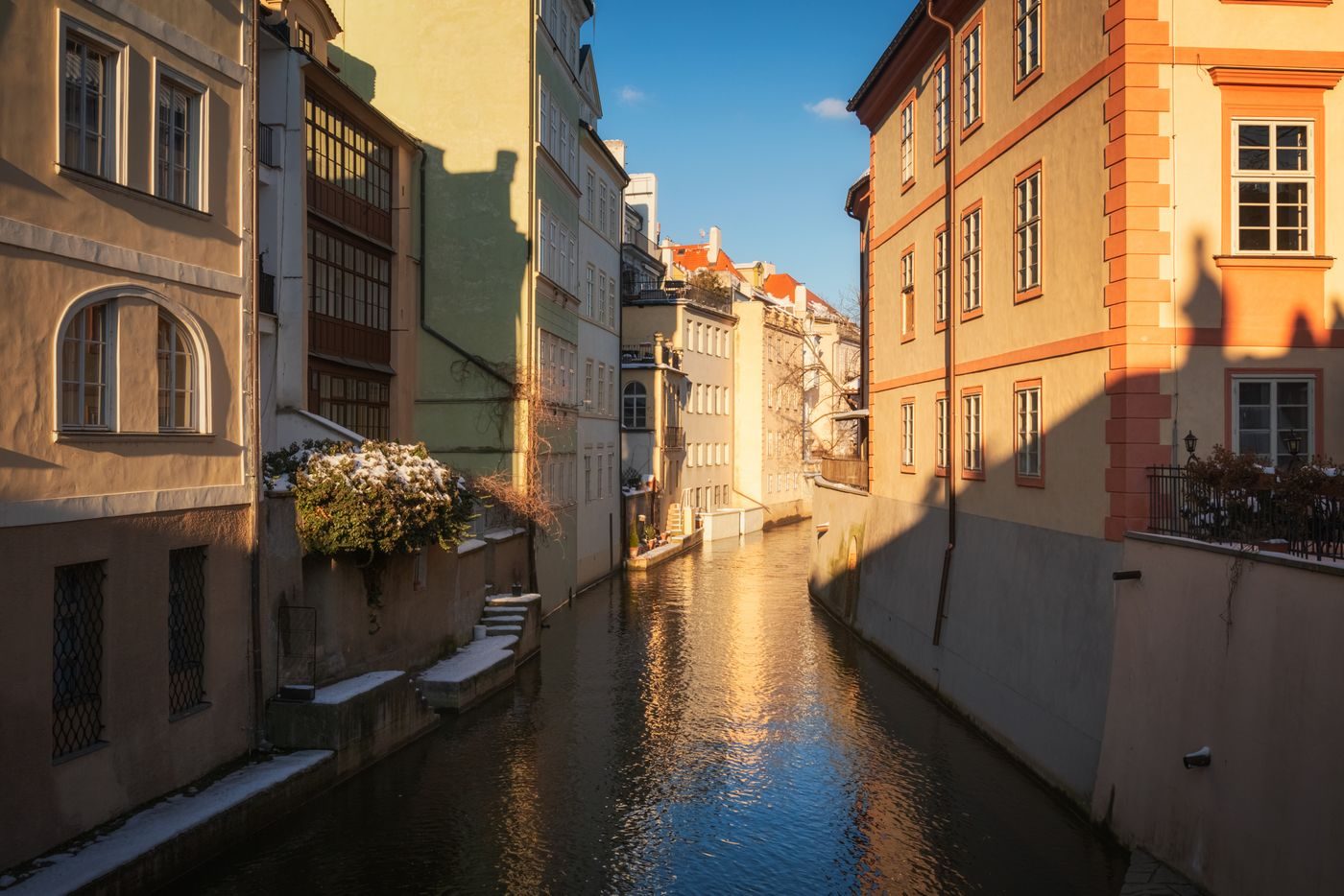 Narrow water channel runs between close colourful Prague buildings.