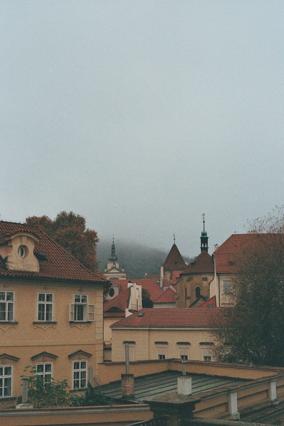 Historic Prague church architecture and rooftops are visibly present in a moody city view.