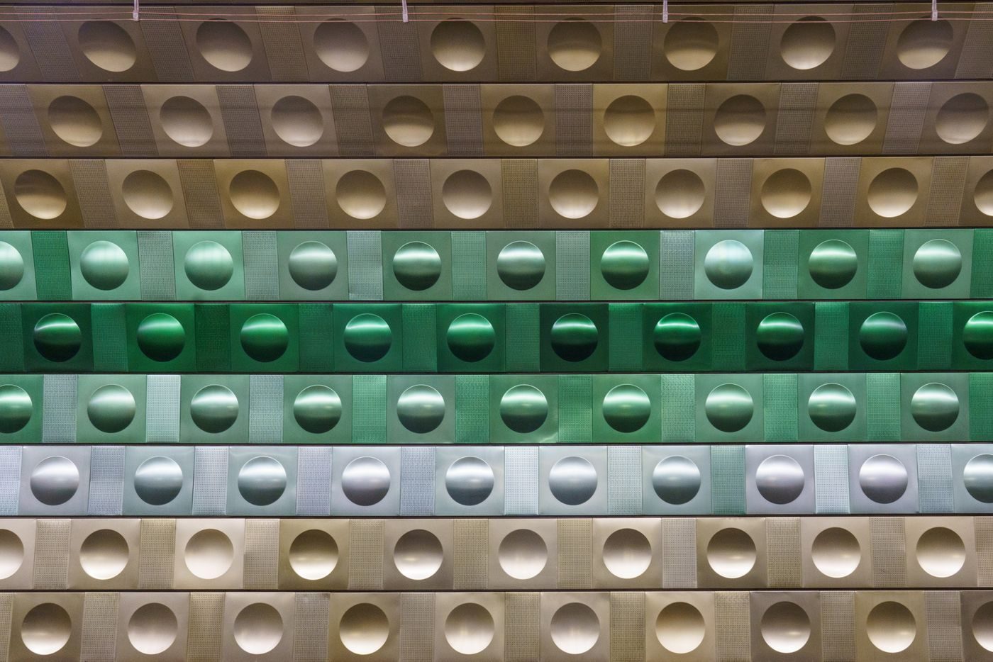 Visual inspection shows a Prague metro wall covered in repeated shaped metallic circular forms with green reflective hues.
