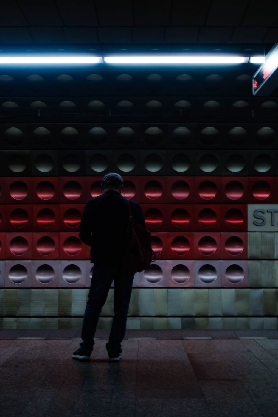 A man waits on an exact Prague metro platform against illuminated wall panels.