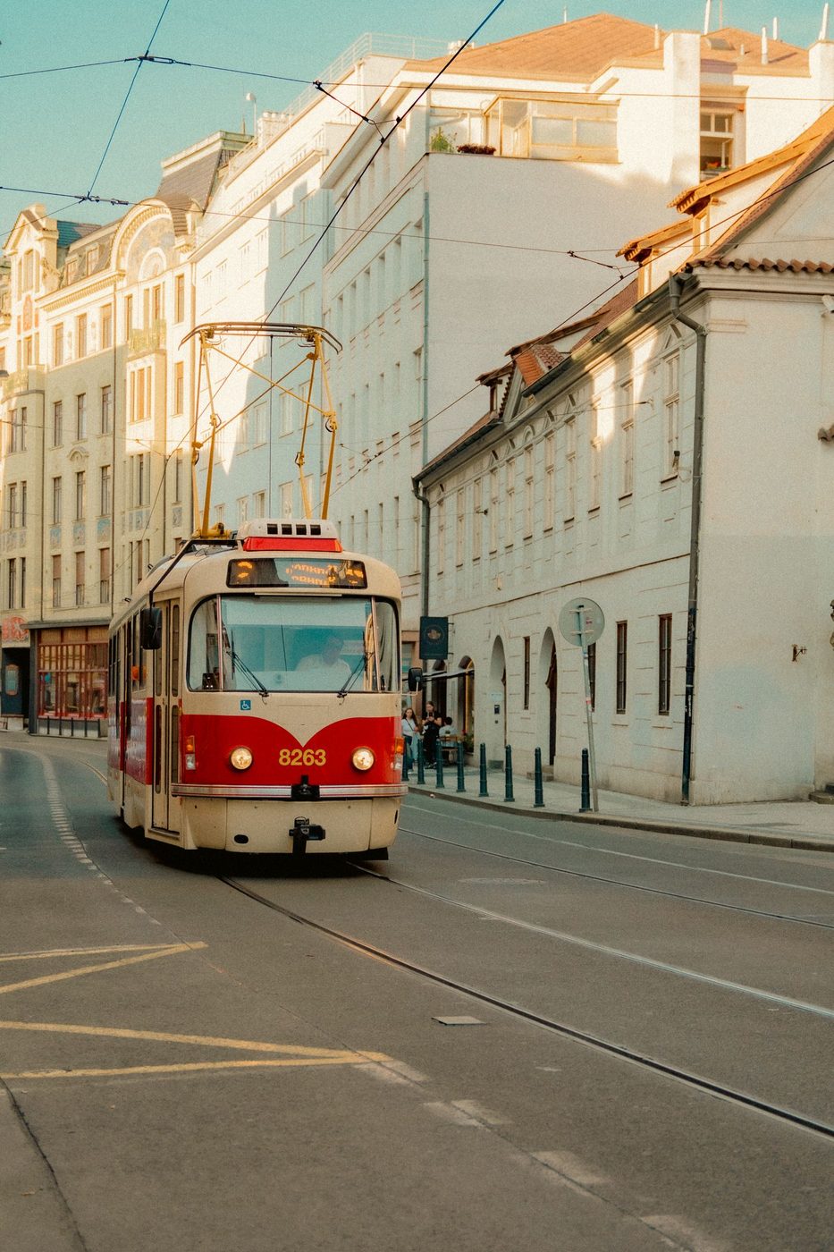 Vertical Prague street frame with a red vintage tram; front route text is too soft to read reliably.
