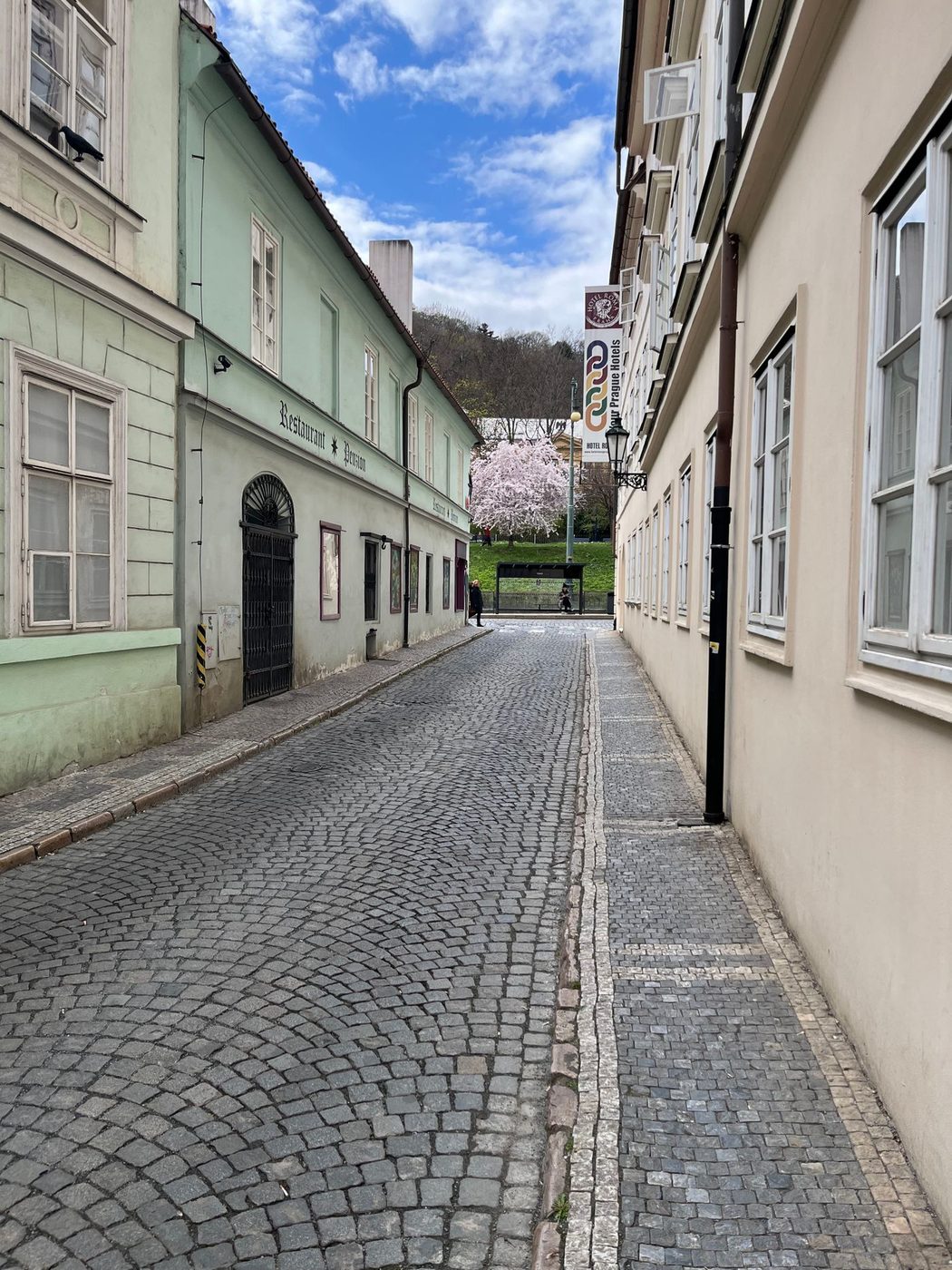 Foreground stones visibly form broad fan/arc courses across a quiet Prague lane.