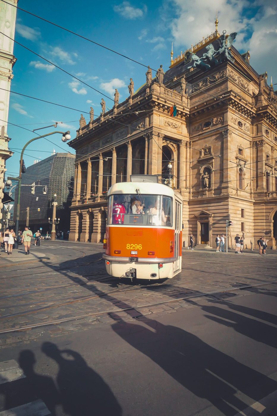 A classic red tram visibly passes the exact National Theatre in daylight.