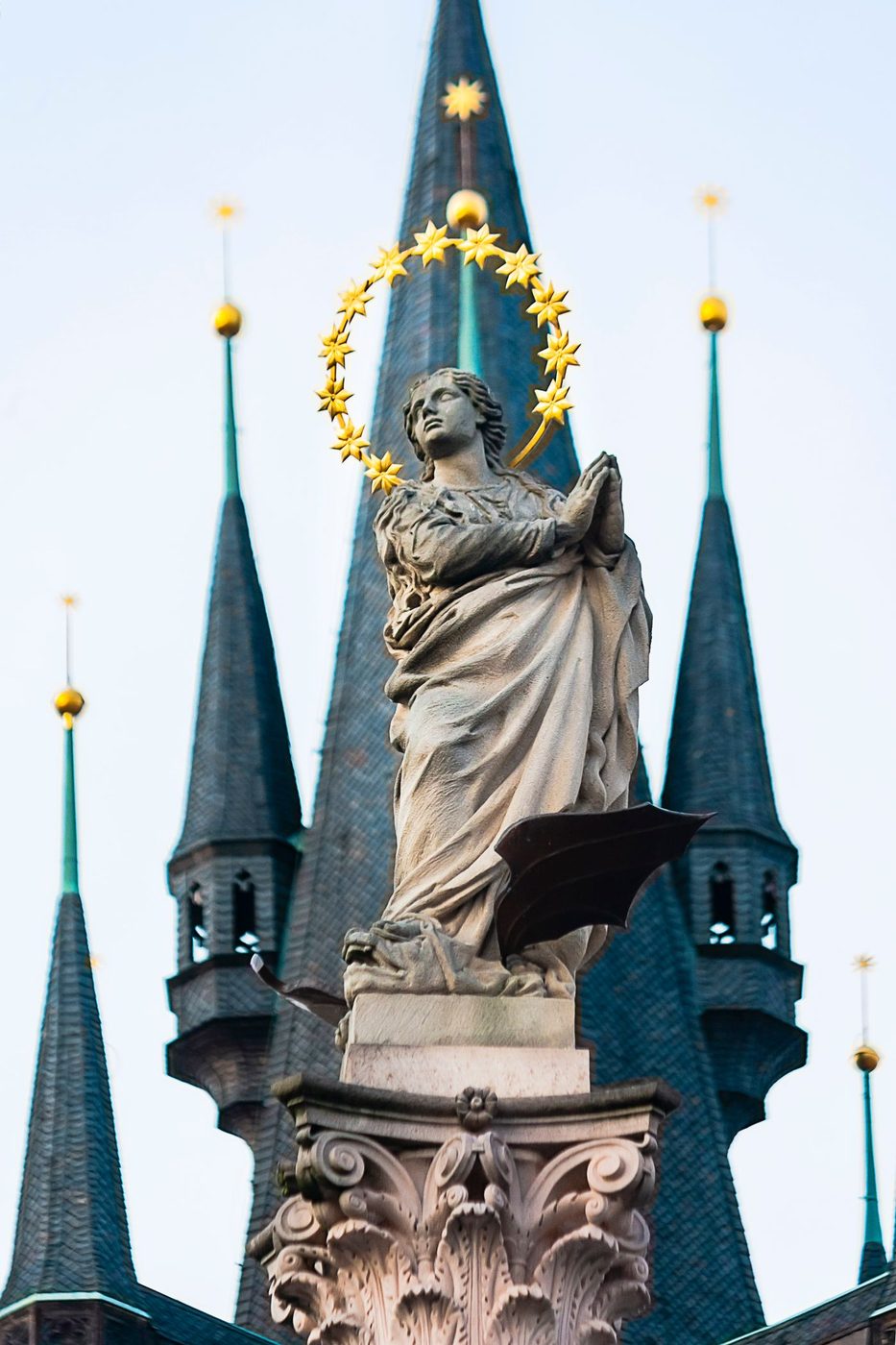 Virgin Mary with halo is visibly atop an ornate column in Prague’s Old Town Square, with Gothic spires behind.
