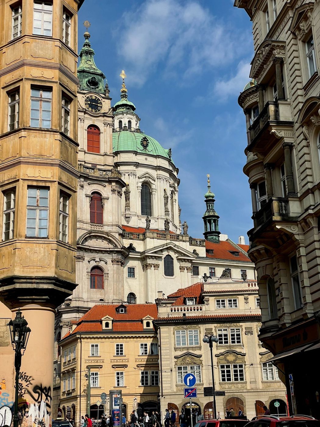 Vertical street view visibly layers the green dome and neighboring tower above Malá Strana façades.