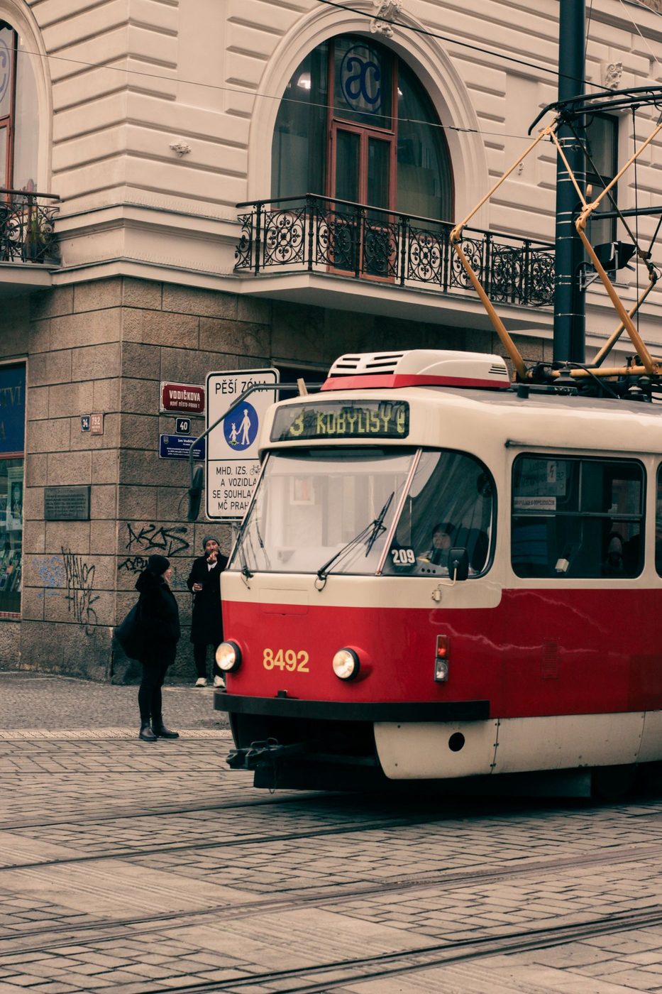 Classic red Prague tram fills a vertical street frame; the route display is not confidently readable as 5.